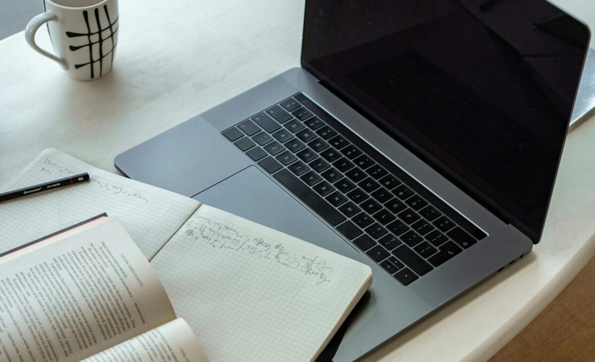 a Table with a book, note block, laptop and a cup of coffee.